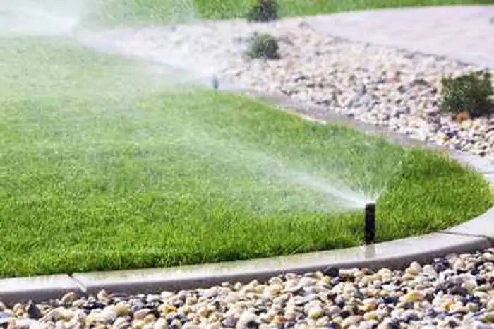 Sprinkler heads watering a lawn beside a gravel and stone border